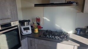 A modern kitchen with a built-in oven, a gas stove, and a microwave. - Chambre avec cuisine équipée sur demande (Figeac)