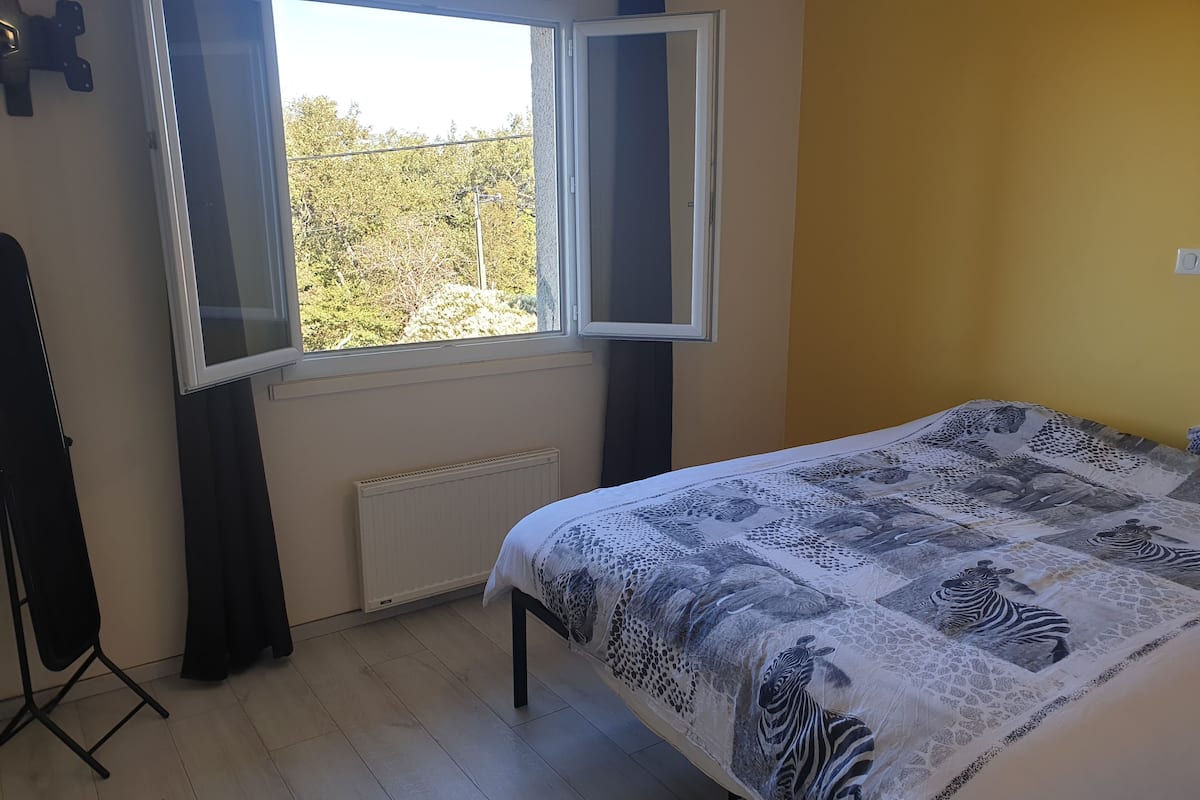 A bedroom with a bed, a radiator, a window, and a view of trees outside.