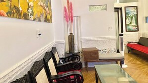 Uma sala de estar com um quadro grande, um vaso de vidro com penas cor-de-rosa, um banco, um sofá e uma mesa.