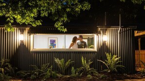 A couple kissing in front of a lit window with a framed picture. - Upon a Star - Welcoming you to the most charming holiday retreat, nestled in the picturesque village of Wandiligong, Victoria. (Wandiligong)