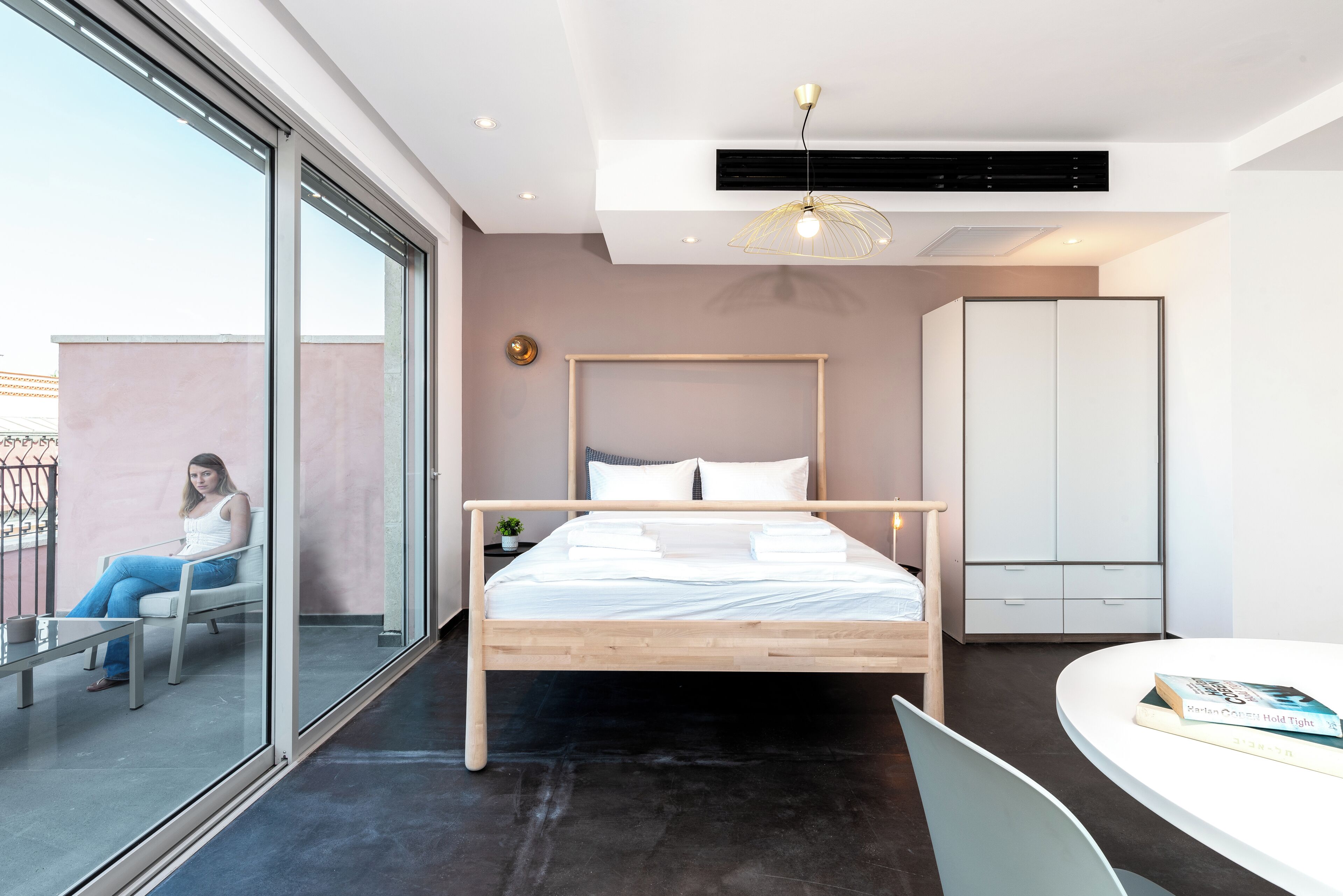 Ein modernes Schlafzimmer mit einem hölzernen Bett, einem weißen Kleiderschrank und einer Glaswand mit Blick auf einen Balkon.