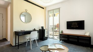 Un salon moderne avec un bureau noir, une chaise blanche et une table ronde sur laquelle est posé un livre ouvert. Un téléviseur est fixé au mur, et un banc est adossé au mur.