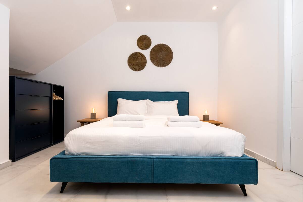 A modern bedroom with a large bed, dark blue headboard, white bedding, and decorative wall art.