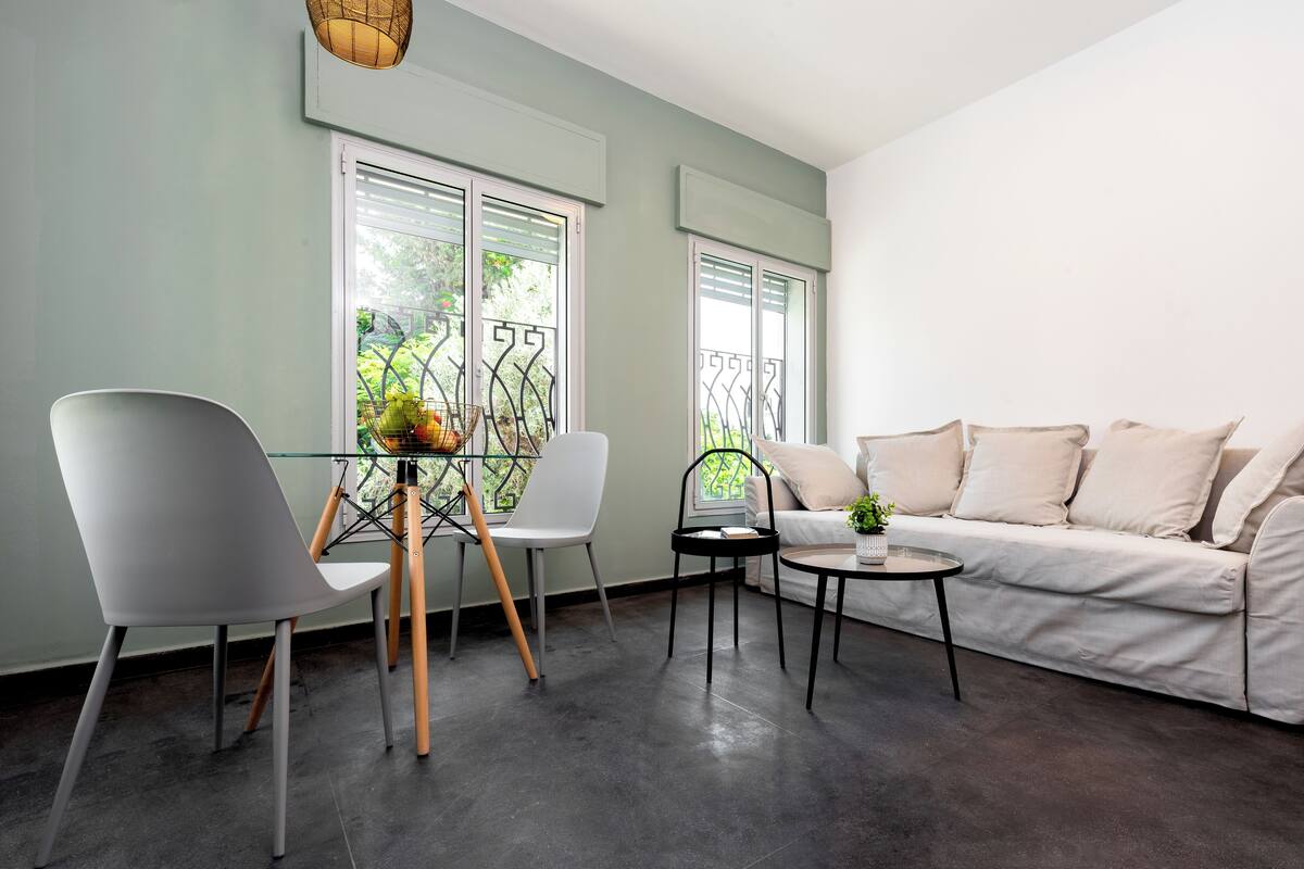 A modern living room with a sofa, two white chairs, a glass table, and a small round table.