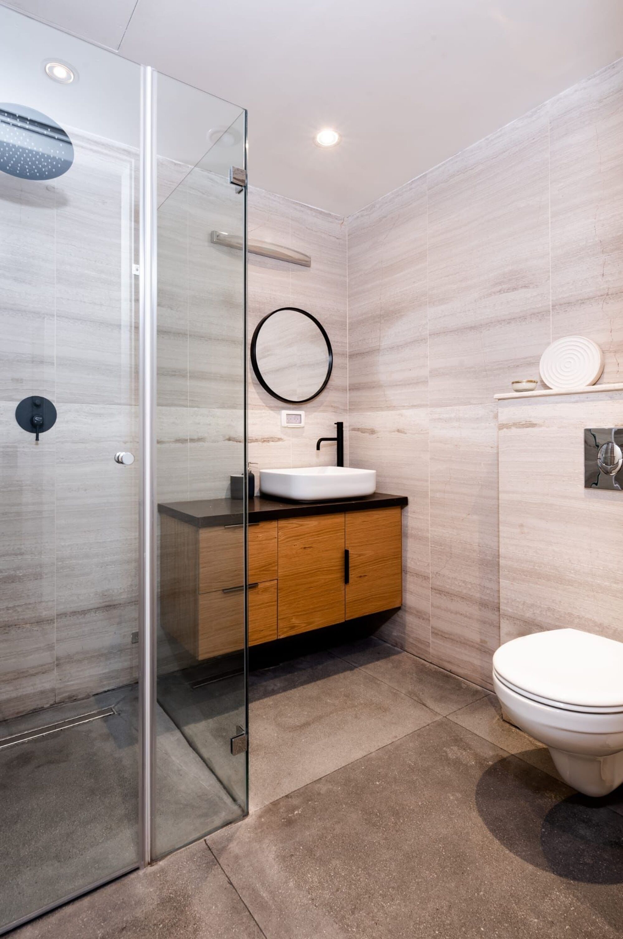 Un baño moderno con ducha de vidrio, tocador de madera con lavamanos blanco y un inodoro.
