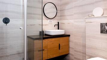 Un baño moderno con ducha de vidrio, tocador de madera con lavamanos blanco y un inodoro.