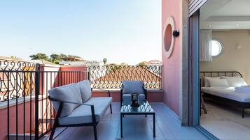 A balcony with a sofa and a table, a bed inside the room, and a view of the cityscape.