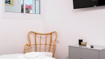 Una cama bien hecha con toallas blancas dobladas, un mueble gris con un cuenco y un control remoto, y un cartel enmarcado en la pared.