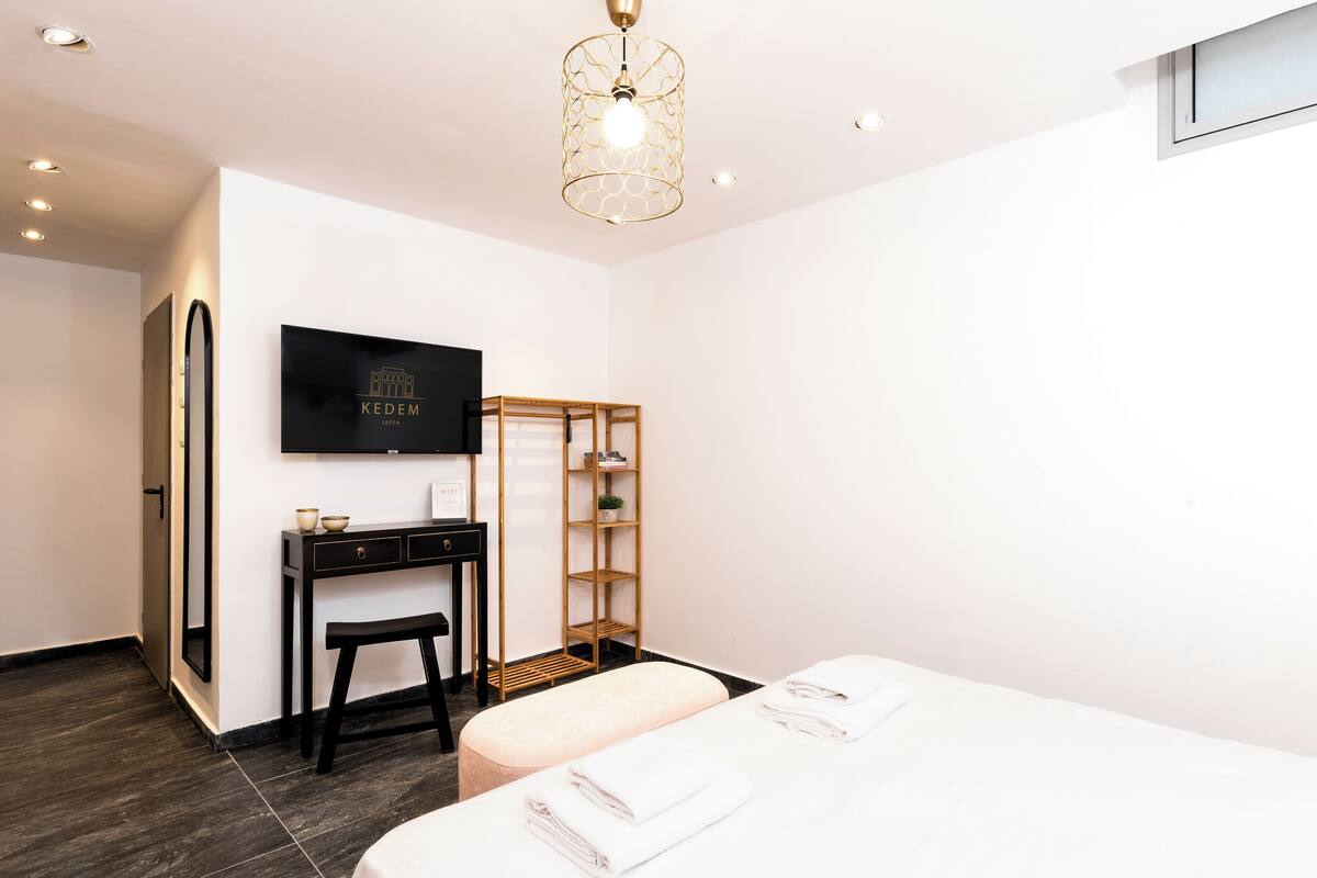 A modern hotel room with a bed, a desk, a chair, a wardrobe, and a television on the wall.