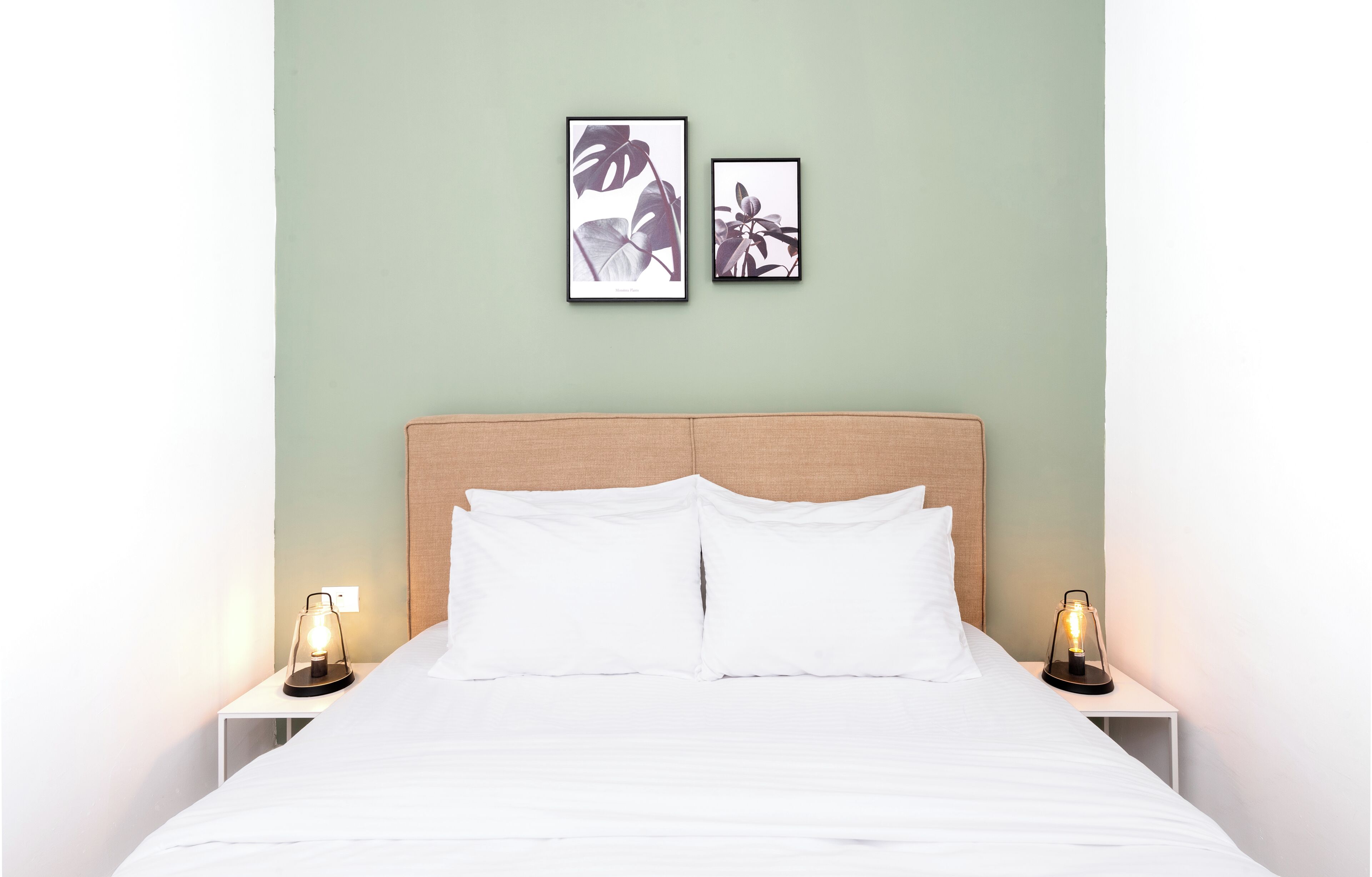 A neatly made bed with white linens, two bedside tables with lamps, and two framed pictures on the wall.
