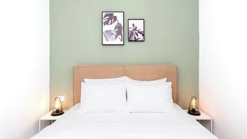 A neatly made bed with white linens, two bedside tables with lamps, and two framed pictures on the wall.