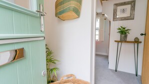 Un corridoio con una porta verde, un arazzo, un quadro incorniciato, un tavolino con una pianta e una borsa tessuta.