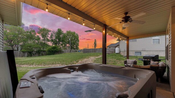 Un bain à remous installé sous un patio couvert, avec vue sur un jardin et un coucher de soleil.