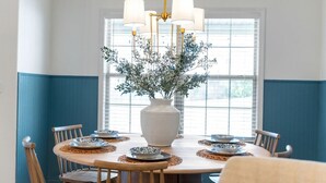 Un coin repas avec une table ronde, des chaises, un vase agrémenté de plantes et un lustre.