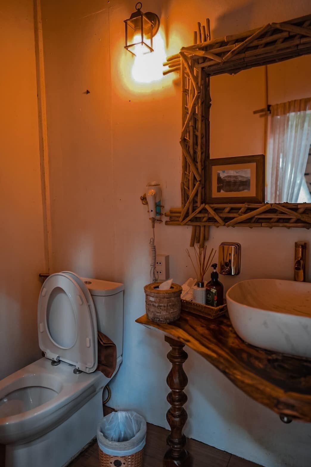 Ein Badezimmer mit Toilette, einem Holzboden mit Waschbecken, einem Spiegel und einer Wandleuchte.