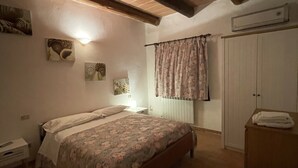 Un dormitorio con cama, mesita de noche, silla, armario y aire acondicionado instalado en la pared.