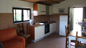 Una cocina compacta con armarios blancos, techo de madera, una mesa de comedor con sillas y una ventana con persianas.