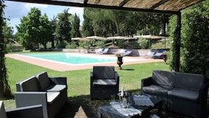 Un patio exterior con mobiliario de mimbre, una piscina y sombrillas.