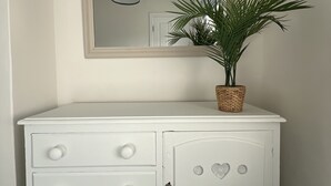 A white dresser with drawers and a cabinet, a mirror above it, and a potted plant on top. - Train Station Cottage Taunton - Walk to town, pet friendly! (Taunton)