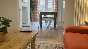 A living room with a wooden coffee table, a patterned rug, a sofa, and a dining area with a table and chairs. - Train Station Cottage Taunton - Walk to town, pet friendly! (Taunton)