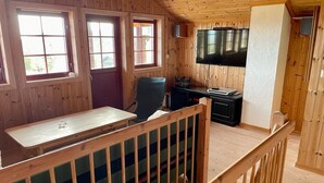 A wooden cabin interior with a dining table, chairs, a TV, and a staircase.