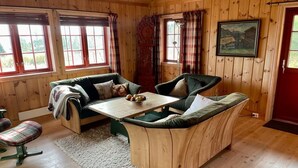 A cozy cabin interior with a wooden floor, a sofa, a dining table, and a chair.