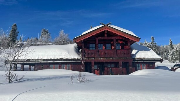 A red wooden building with a snow-covered roof, surrounded by snow-covered trees.