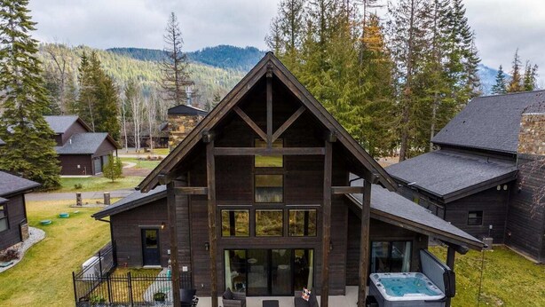 A modern log cabin with a large deck, outdoor seating, and a hot tub.