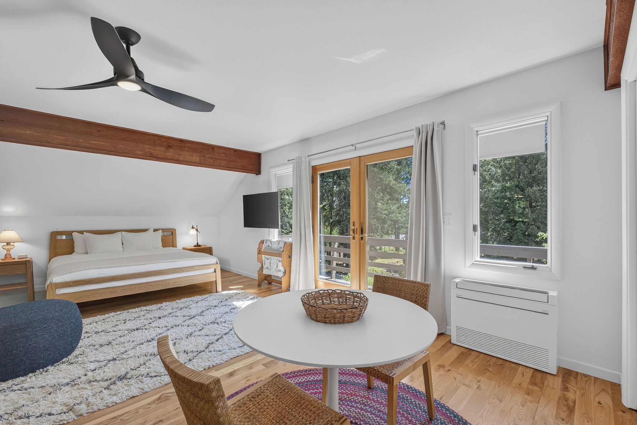 A bedroom with a bed, a ceiling fan, a TV, a window, and a dining area with a table and chairs.