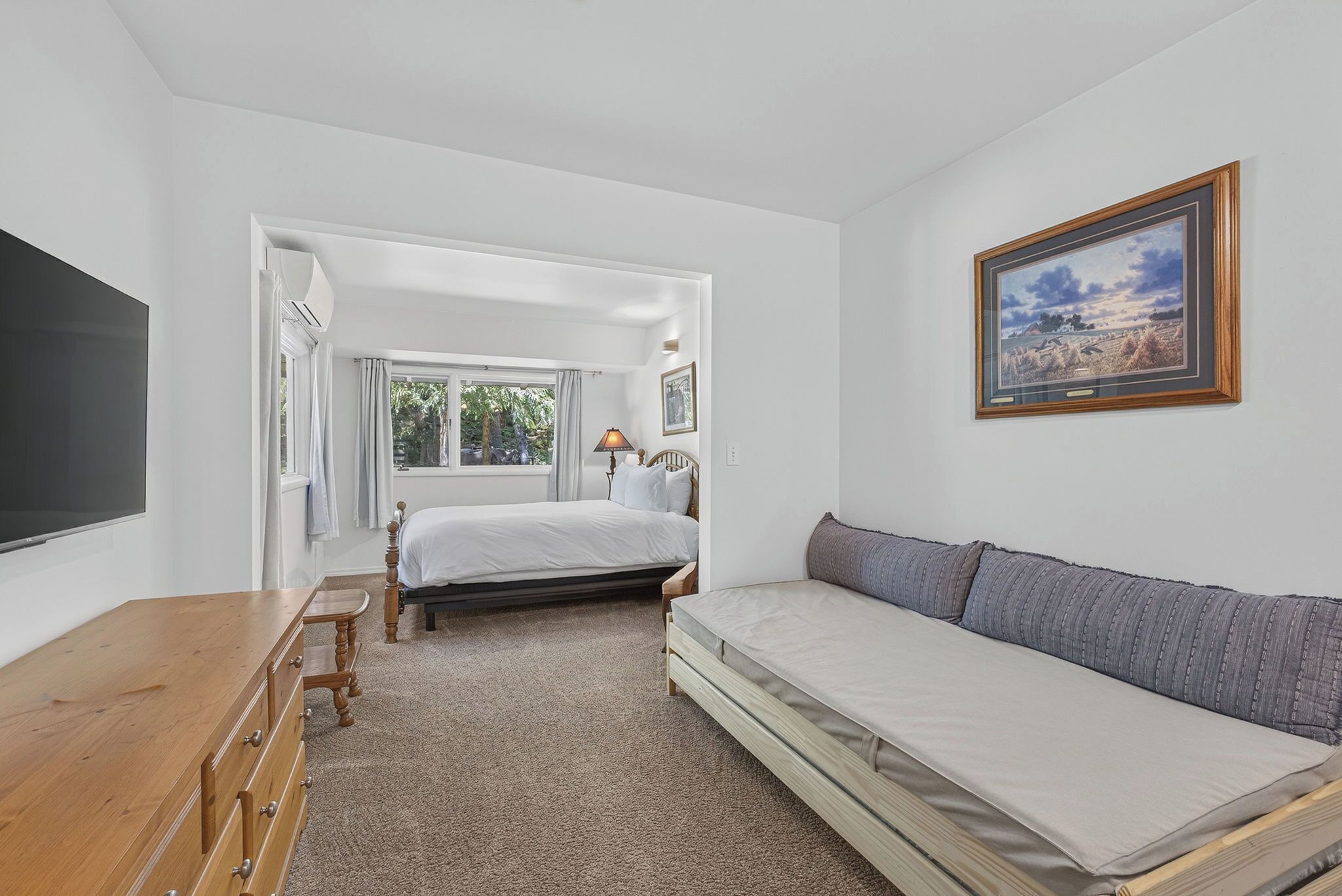 A bedroom with a bed, a sofa, a wooden dresser, a TV, and a framed picture on the wall.