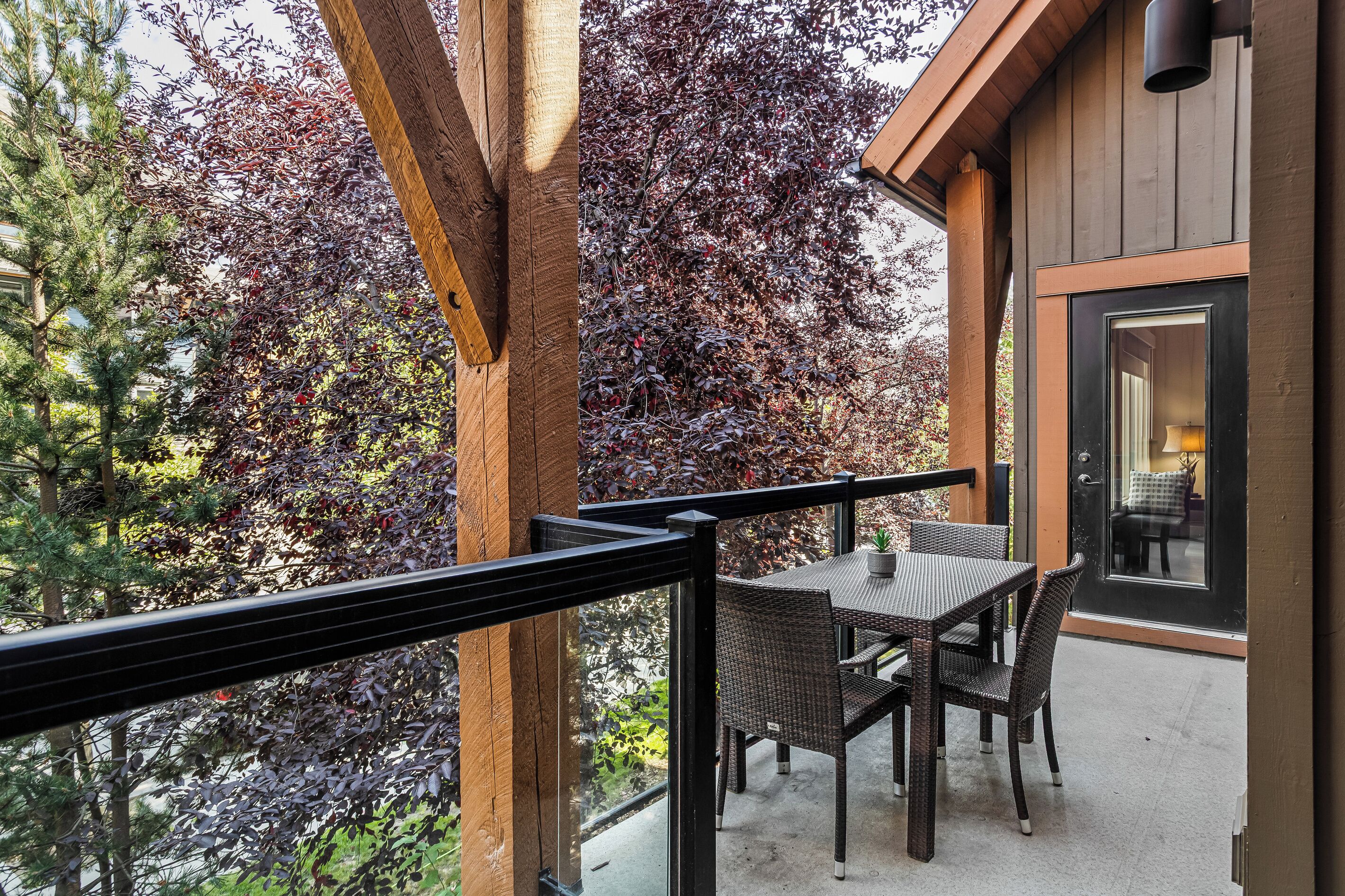 A balcony with wicker furniture, a glass door leading inside, and a view of trees with red leaves.