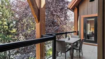 A balcony with wicker furniture, a glass door leading inside, and a view of trees with red leaves.