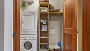 A laundry room with stacked washers and dryers, shelves with folded towels, and baskets. - Gorgeous Mountain Condo - Pool & Hot Tub (Canmore)