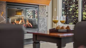 A cozy indoor setting with a fireplace, a table with glasses, and a view of greenery outside.