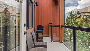 A balcony with wicker furniture, a grill, and a view of a mountain town. - Gorgeous Mountain Condo - Pool & Hot Tub (Canmore)