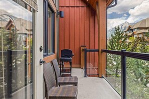 A balcony with wicker furniture, a grill, and a view of a mountain town.