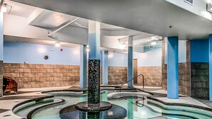 A spa area with a central water feature, stone walls, and a tiled floor. - Gorgeous Mountain Condo - Pool & Hot Tub (Canmore)