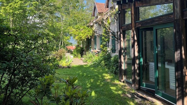 Una casa con terraza de madera, un jardín con diversas plantas y vistas a un lago.