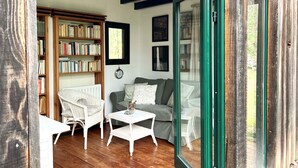 Un salón acogedor con una estantería, dos sillas blancas de mimbre, un sofá gris y una pequeña mesa blanca.