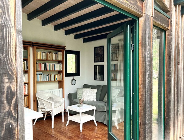 Un salón acogedor con una estantería, dos sillas blancas de mimbre, un sofá gris y una pequeña mesa blanca.