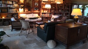 A cozy, well-lit living room with a large sofa, armchairs, and a coffee table. There are bookshelves filled with books and decorative items, and a wooden ceiling. - la Fermette des Petites-haies , un Hymne a la Douceur de Vivre (Lorris)