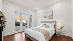Un dormitorio con cama, lámpara de noche, ventana y puerta que da a un espacio exterior.
