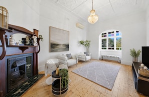 A living room with a fireplace, a large window, a chandelier, and a painting on the wall.
