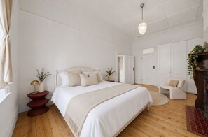 A bedroom with a large bed, a bedside table, a chair, a wardrobe, and a fireplace.