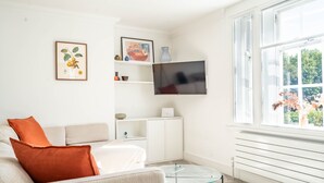 A modern living room with a sofa, a glass coffee table, a flat-screen TV mounted on the wall, and a window with a view of greenery. - Apartment 8 - Bootham House - sleeps 2 guests  in 1 bedroom (York)
