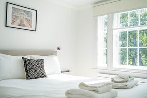 Une chambre d’hôtel avec un lit, un oreiller, un tableau encadré au mur et une fenêtre donnant sur des arbres.