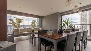 En moderne stue med spiseplads, store vinduer og en balkon med planter.