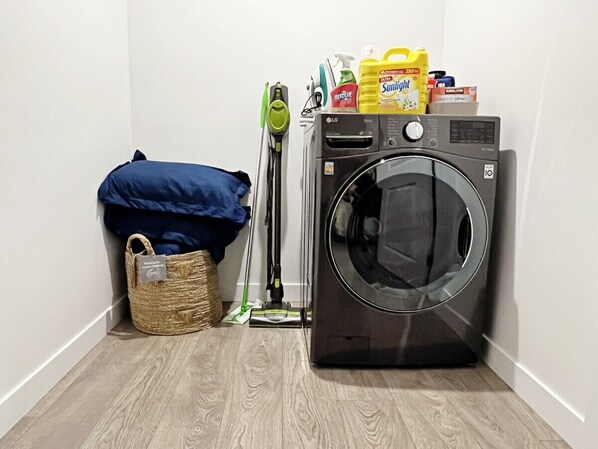 A laundry area with a washing machine, a vacuum cleaner, and cleaning supplies.