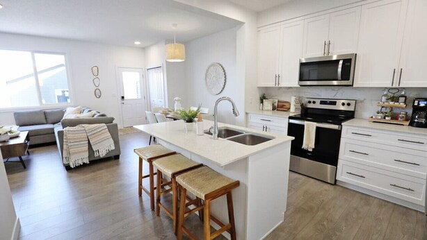 A modern kitchen with white cabinets, stainless steel appliances, and a central island with stools. - BoHo Retreat with King Beds|A/C|Disney+|Near WEM (Edmonton)