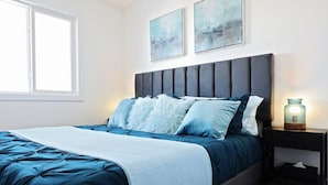 A bedroom with a bed, a nightstand, a lamp, and artwork on the wall. - BoHo Retreat with King Beds|A/C|Disney+|Near WEM (Edmonton)